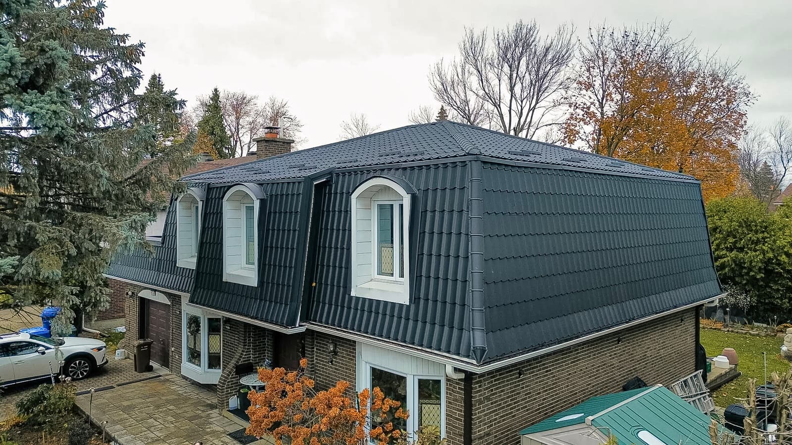 Brick house with a black metal tile-style roof and white dormers.
