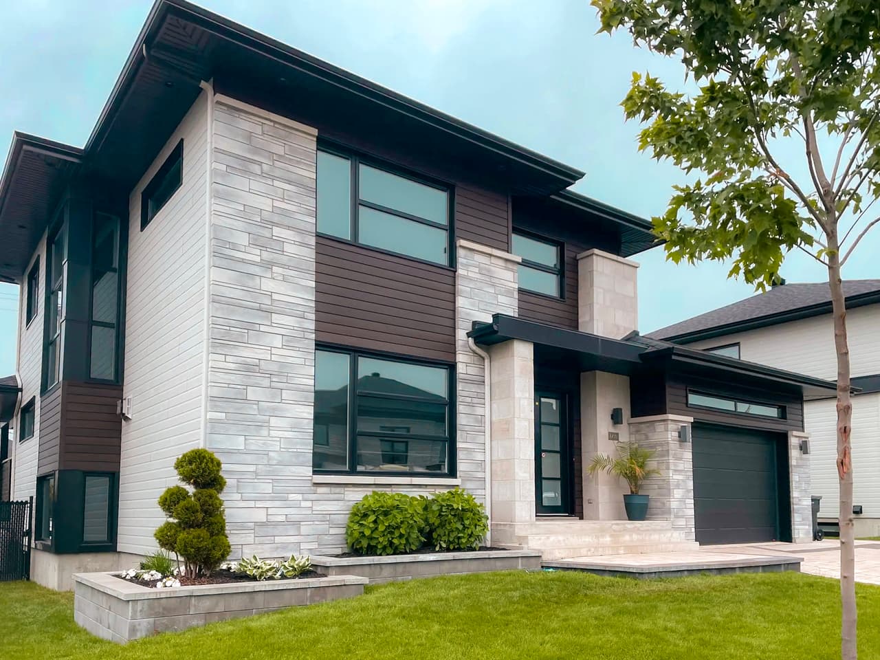 Modern two-story house with gray stone facade, brown wood siding, and integrated black garage
