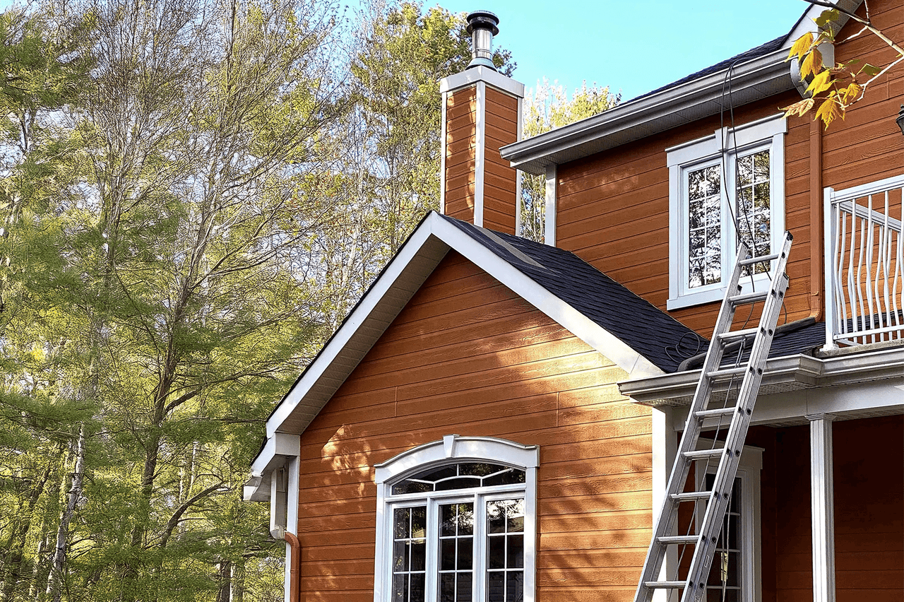 Orange-toned wooden house with chimney, black shingle roof, white balcony, and access ladder on the facade