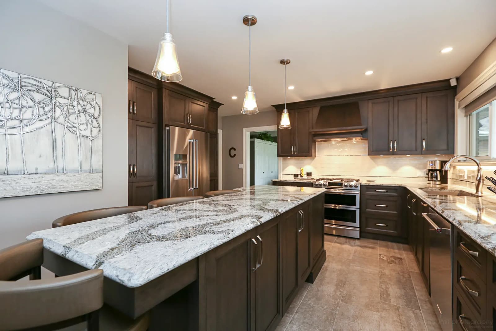 Traditional-looking Montréal kitchen, featuring a spacious central island with a veined granite countertop. The dark wood cabinets and brushed nickel handles add a touch of elegance to the space. The neutral ceramic flooring creates a harmonious backdrop.