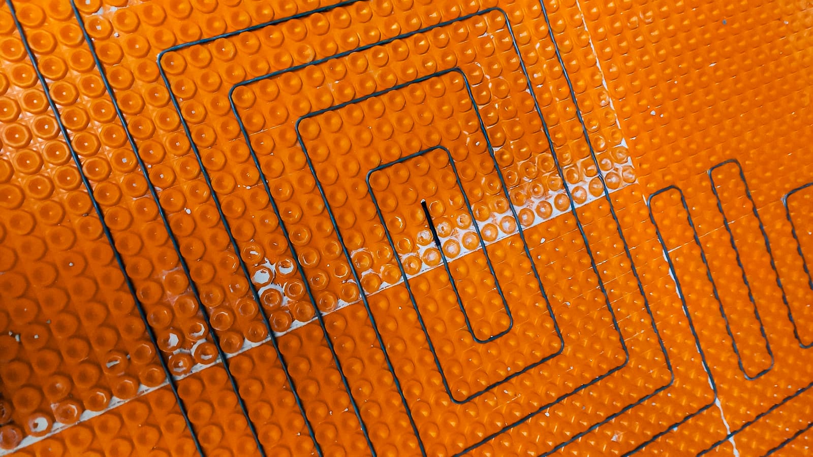  Electric underfloor heating system under installation, with cables embedded in an orange membrane.