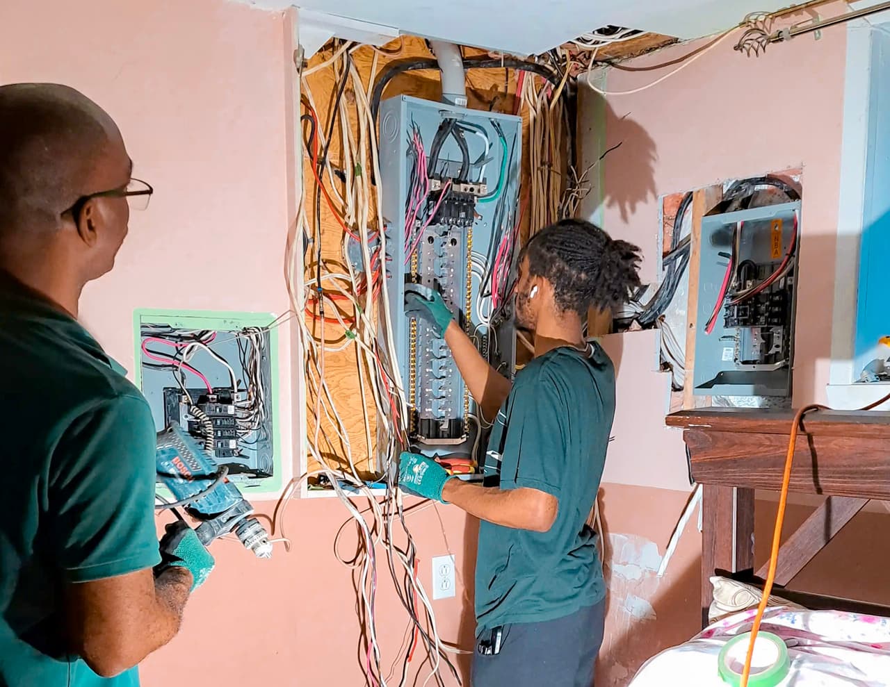 Electricians repairing and reorganizing a residential electrical panel with exposed wiring