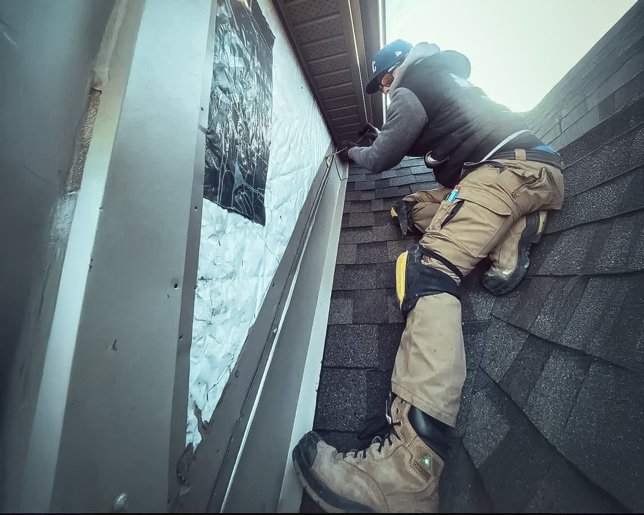 Worker performing installation or repair on a shingle roof, wearing safety equipment.