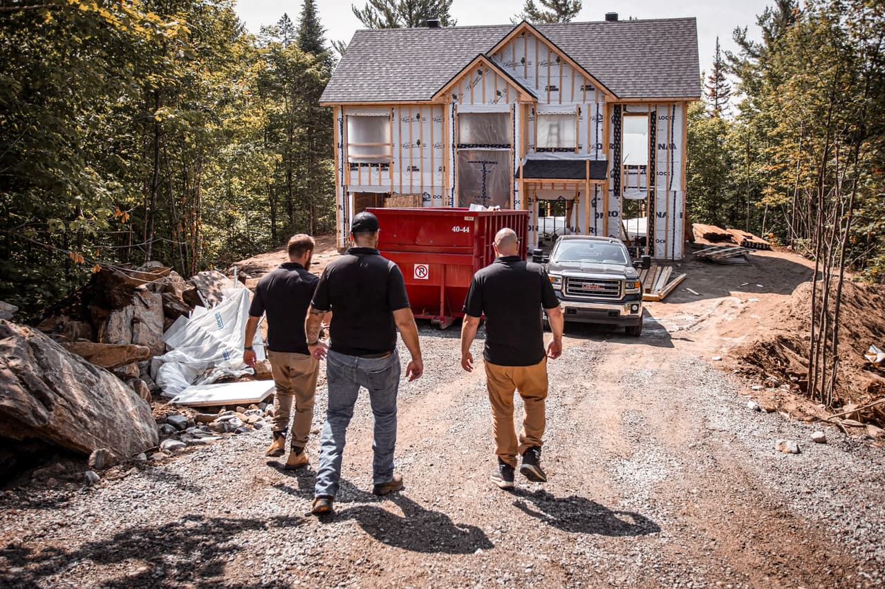 Three professionals inspecting a residential construction site with a house under construction surrounded by greenery.