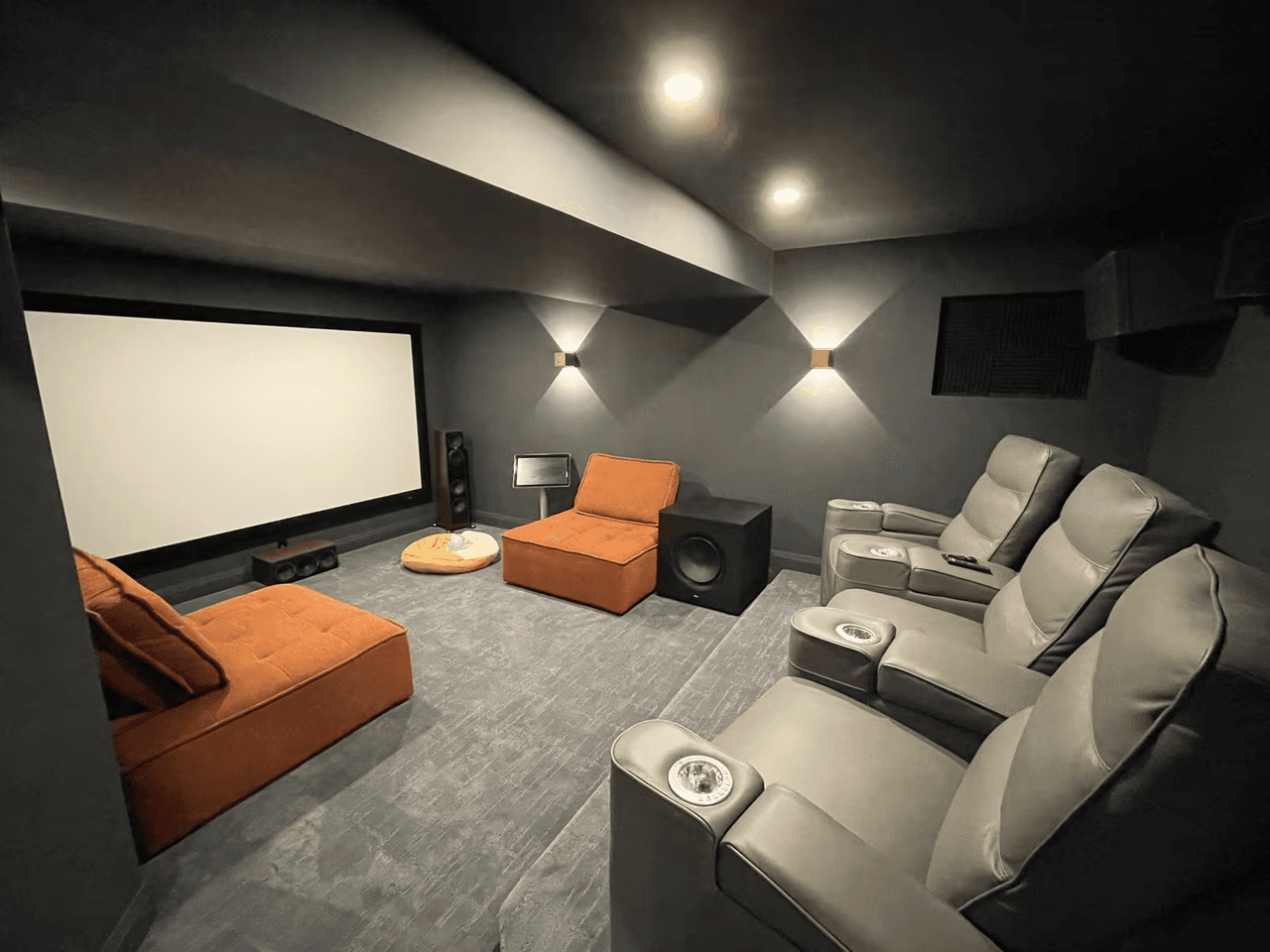 Dark home theater room with large screen, reclining seats, speakers, wall lighting and acoustic walls