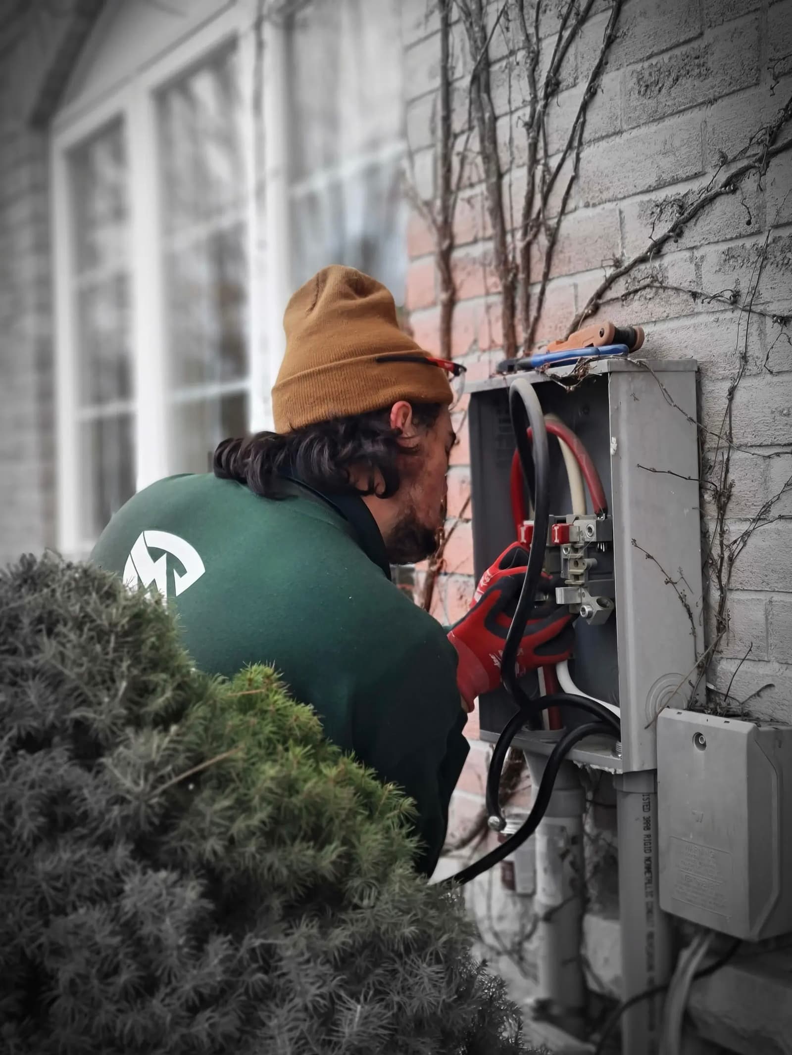 An electrician performing repairs on an outdoor electrical box attached to a brick wall.