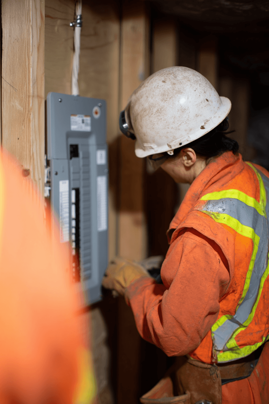 Electrician wearing safety helmet working on an electrical panel inside a wooden construction structure