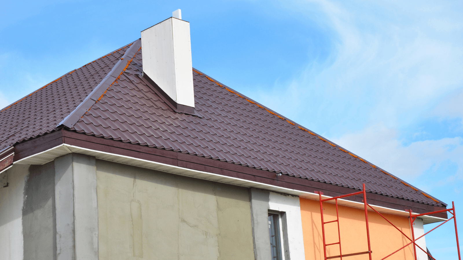 A house under construction with a brown metal roof and a white chimney. The exterior of the house is partially covered with insulation and finishing panels