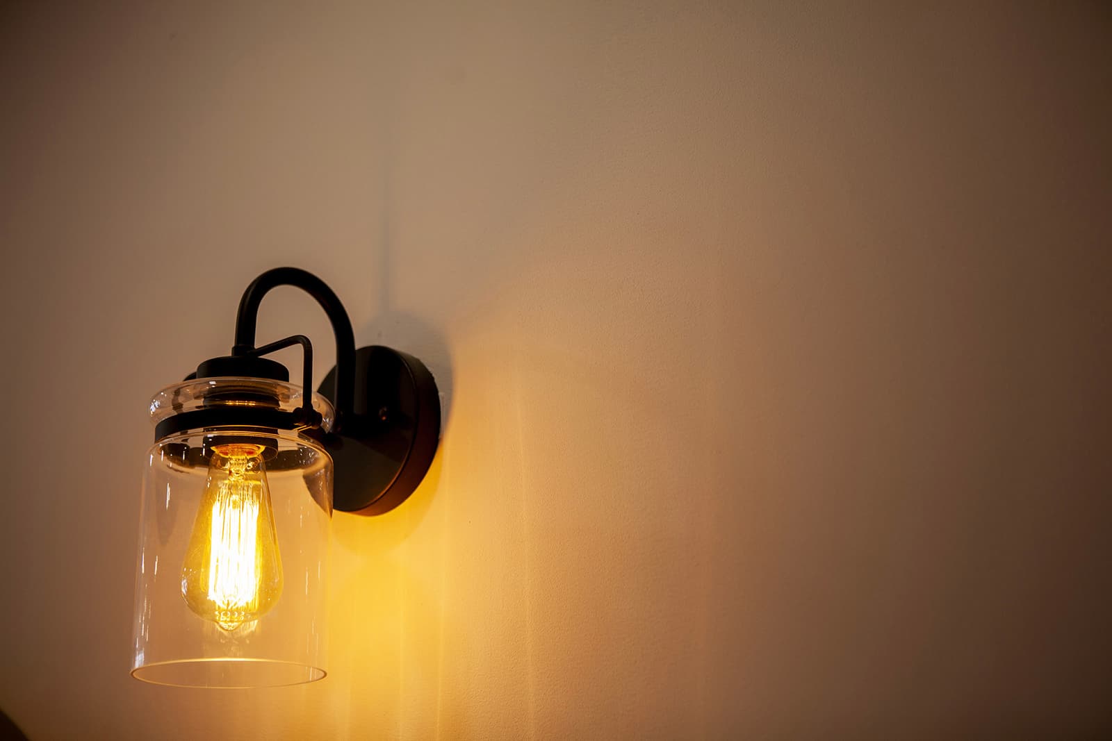 Black wall sconce with lit Edison bulb and clear glass shade emitting warm light