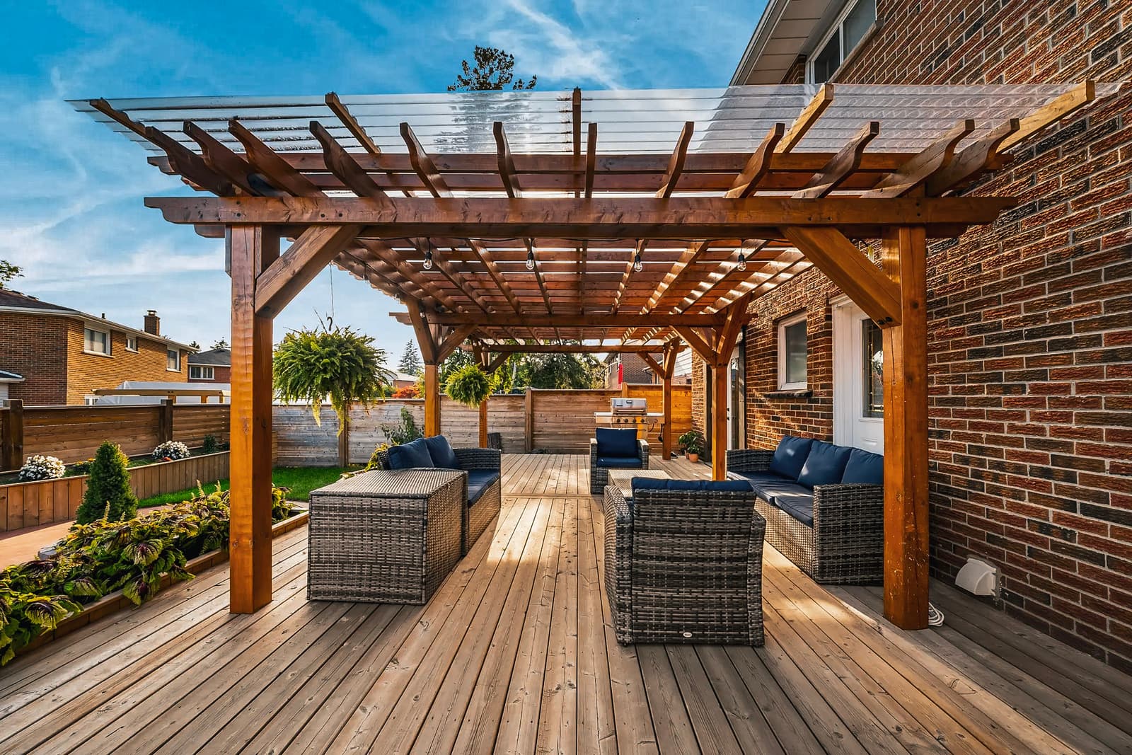 Modern backyard deck with a wooden pergola, rattan furniture, blue cushions, privacy panels, and elegant landscaping.