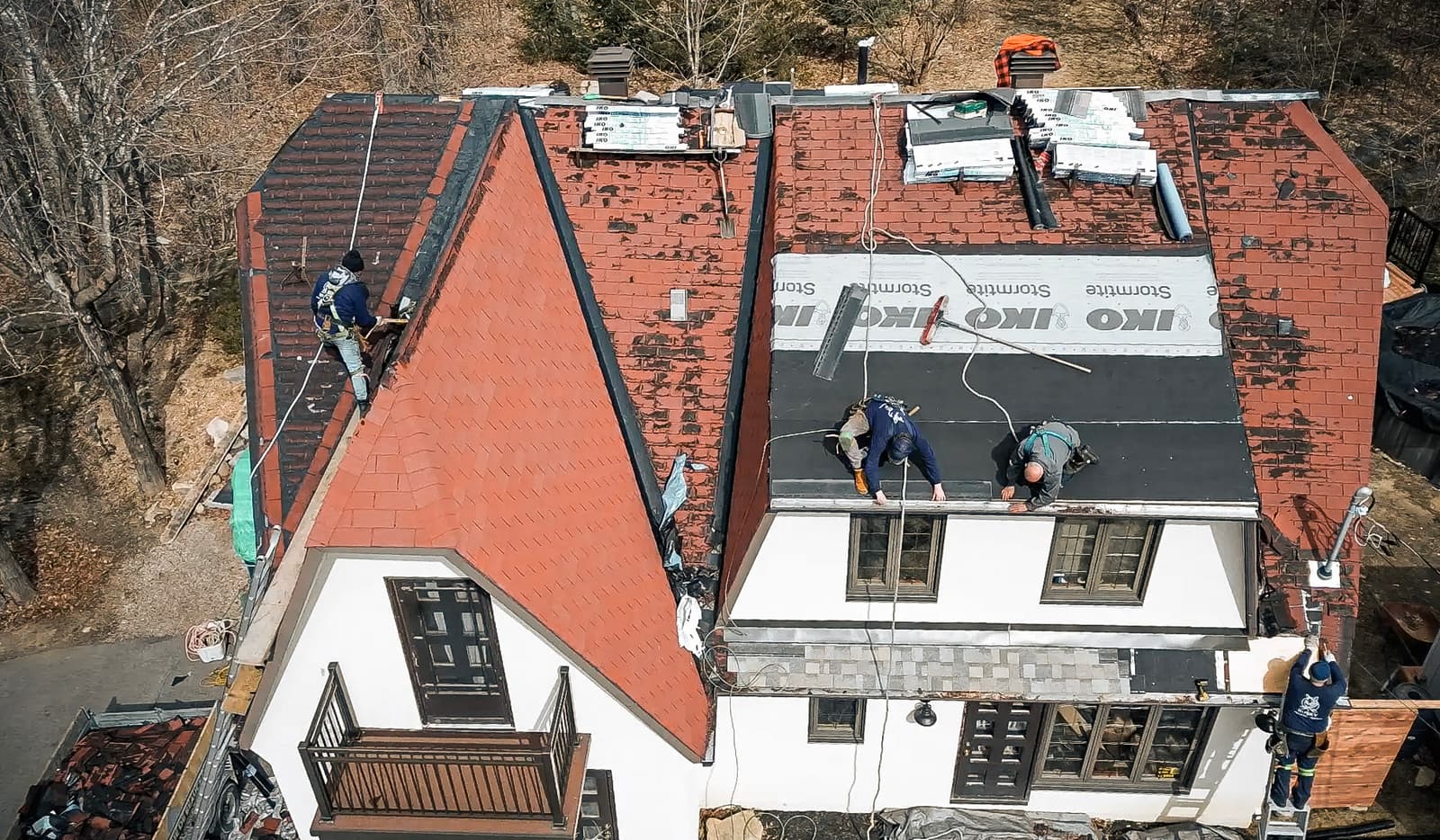 Roof renovation work with red shingles being installed on a multi-story house.