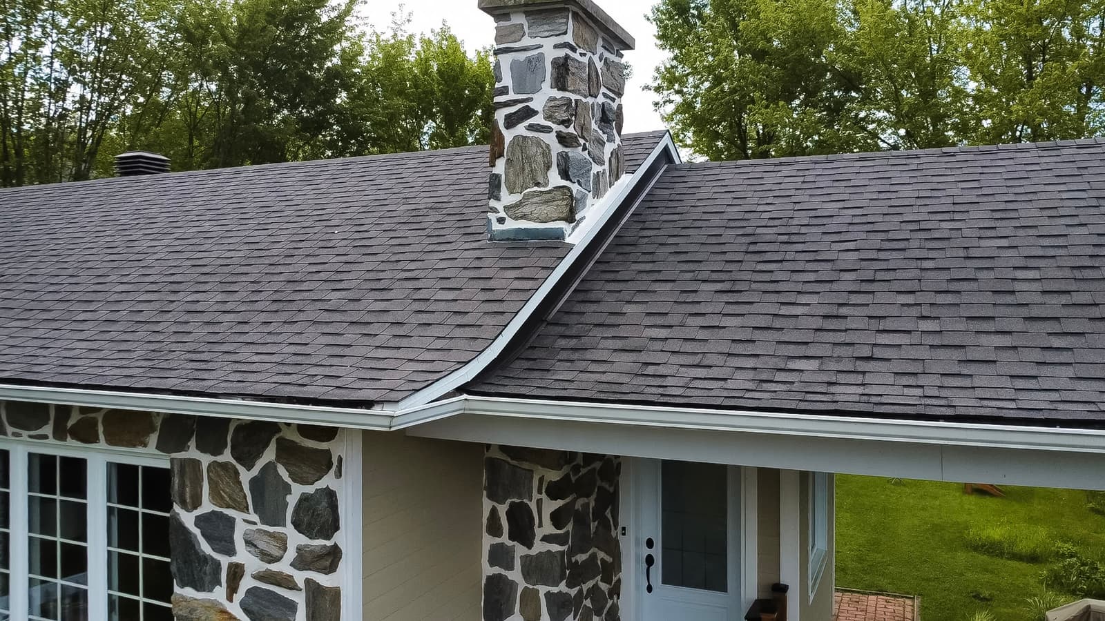 Residential roof covered with gray asphalt shingles and ventilation vents under a clear sky.