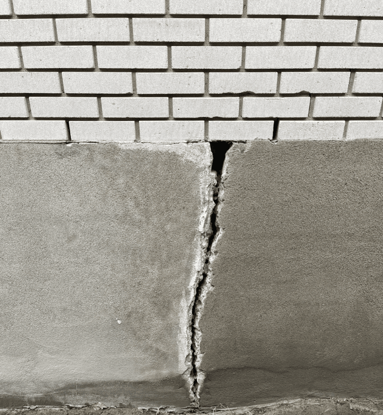 Pronounced vertical crack between concrete foundation and brick wall of a residential house