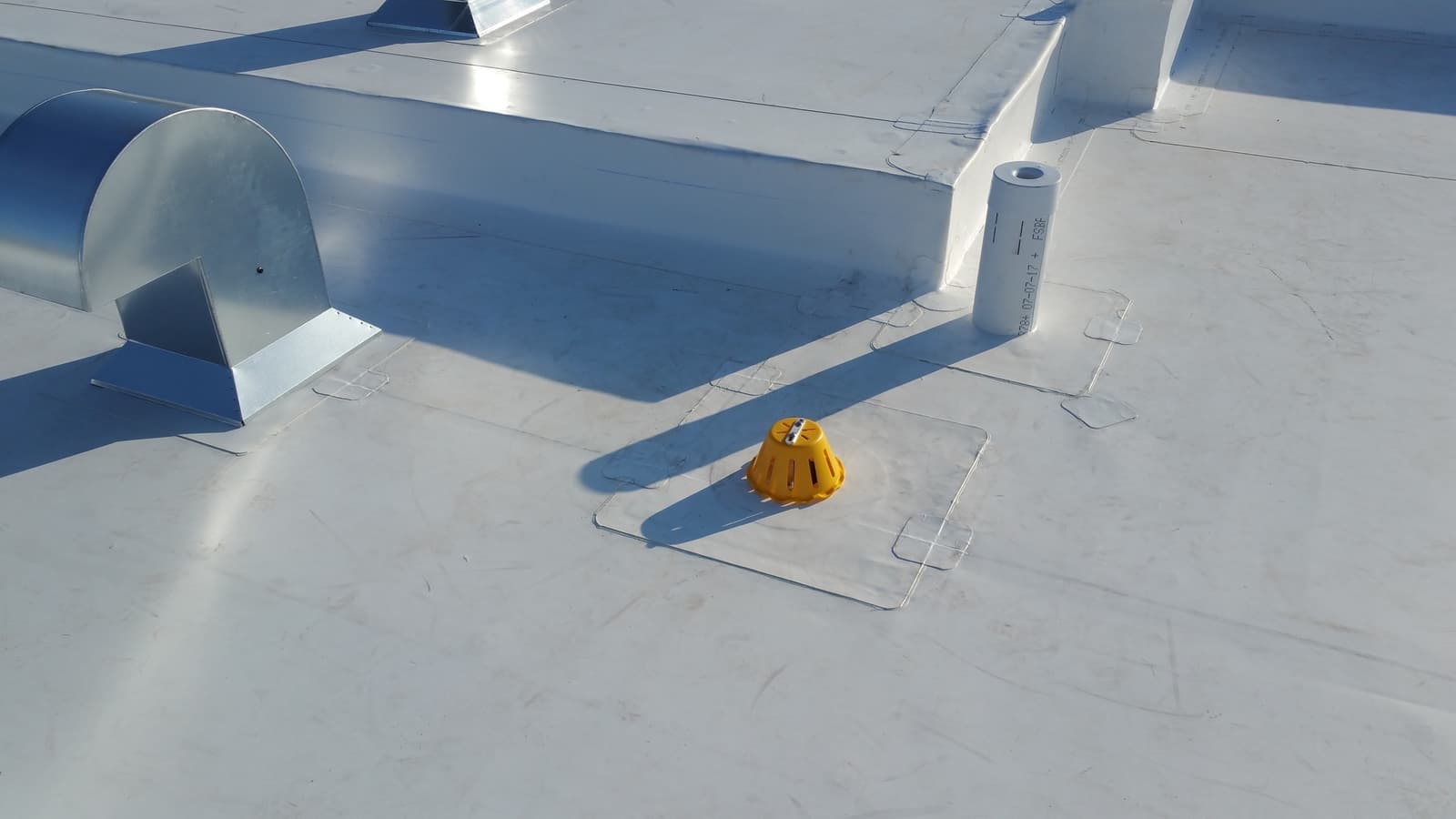 Detail of a flat roof covered with a white membrane, showing ventilation ducts and a yellow roof drain, ensuring proper water management and building ventilation&nbsp;