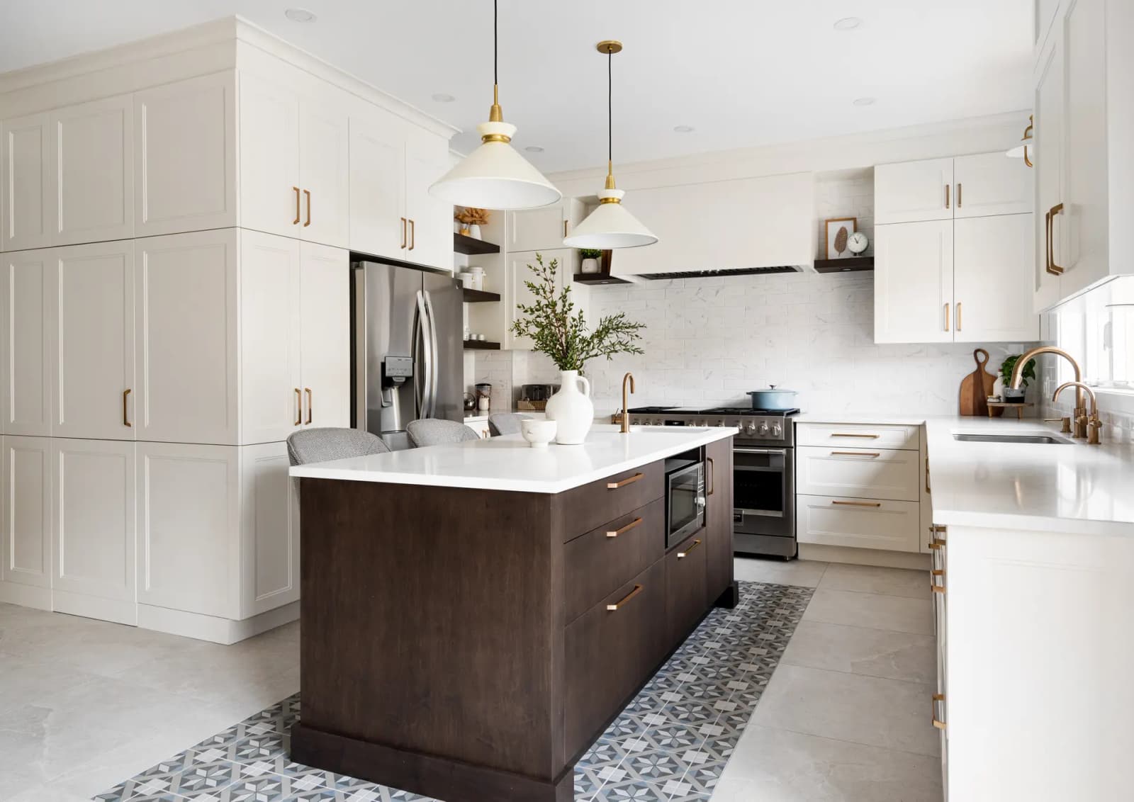 Transitional-style Montréal kitchen, featuring a dark wood centre island with warm-hued drawers and a white quartz countertop. White shaker cabinets and gold handles add a touch of elegance to the space. The geometrically patterned ceramic tile floor adds a touch of sophistication.