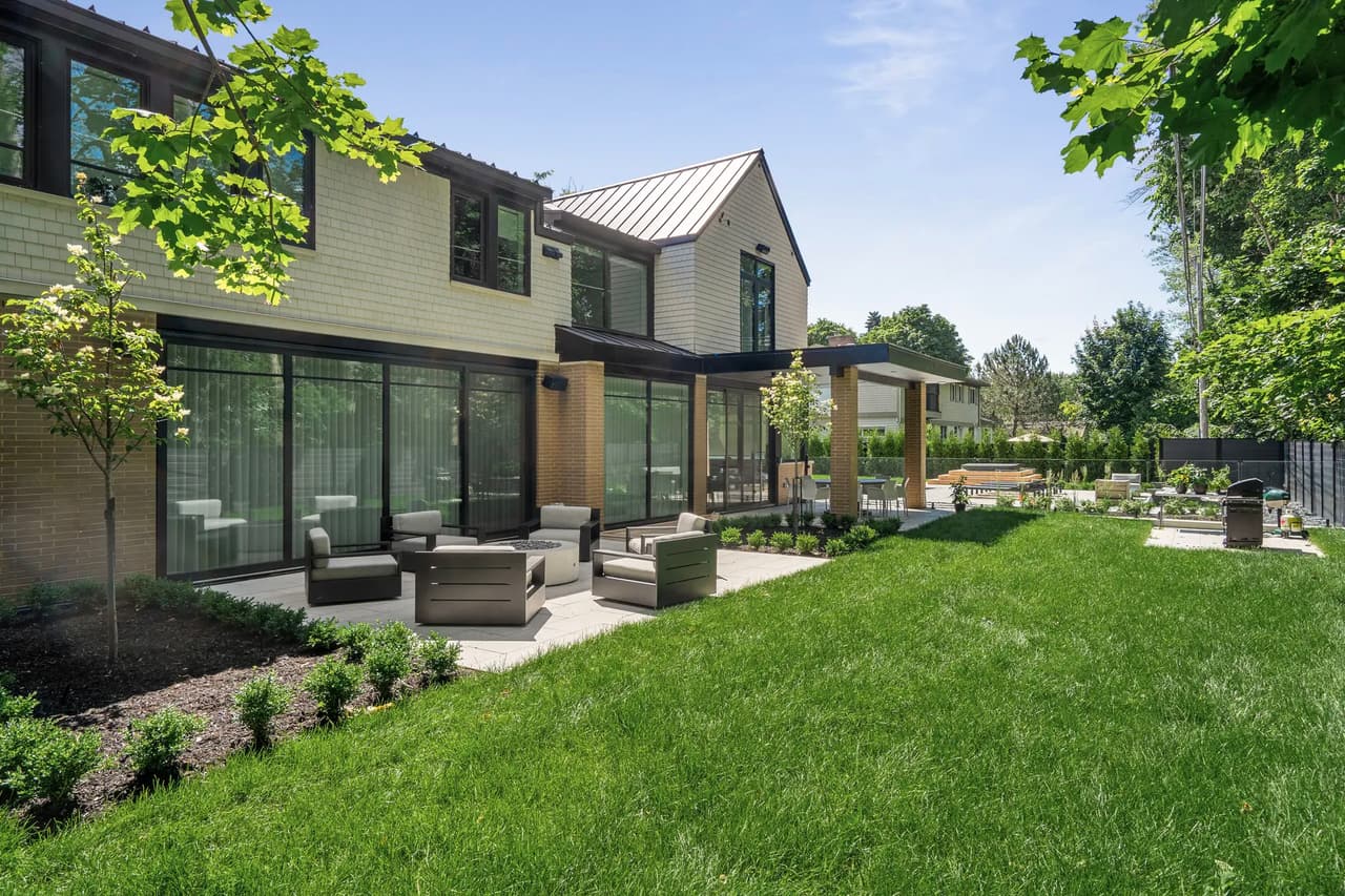 Modern house with a spacious patio, outdoor furniture, well-maintained lawn, and meticulous landscaping, surrounded by trees.