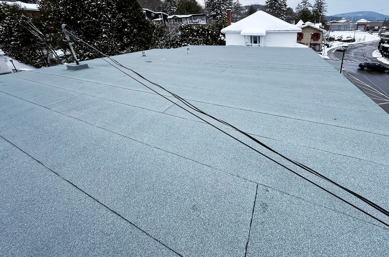 Flat roof covered with a gray elastomeric membrane in winter with visible electrical cables.