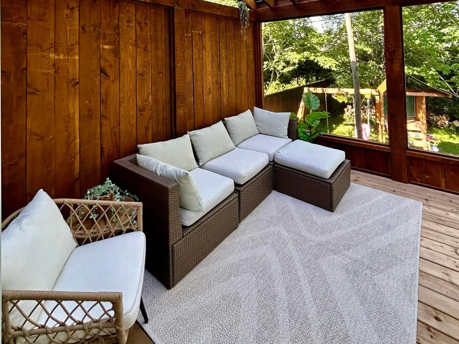 Wooden pergola with a covered deck, outdoor furniture, and white cushions in a natural setting.