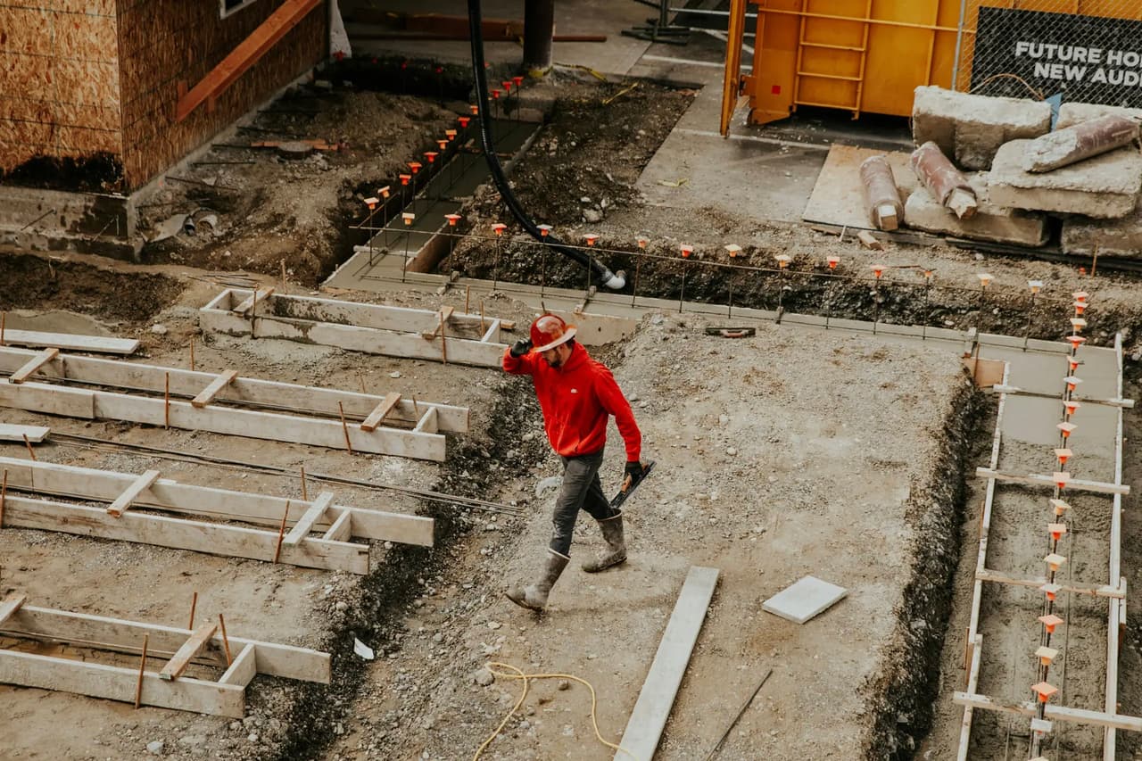 Construction worker walking through an excavation with formwork and rebar for building foundation.