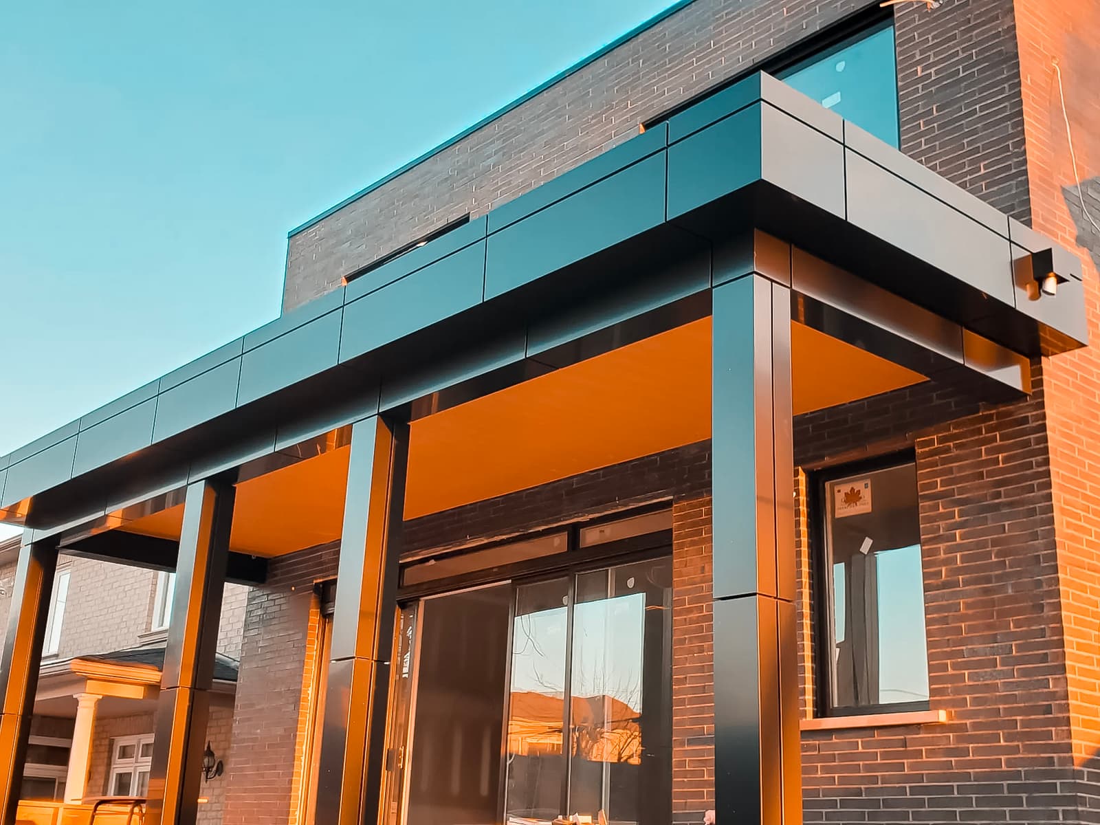 Modern entrance of a dark brick house with a black metal structure and wooden ceiling.