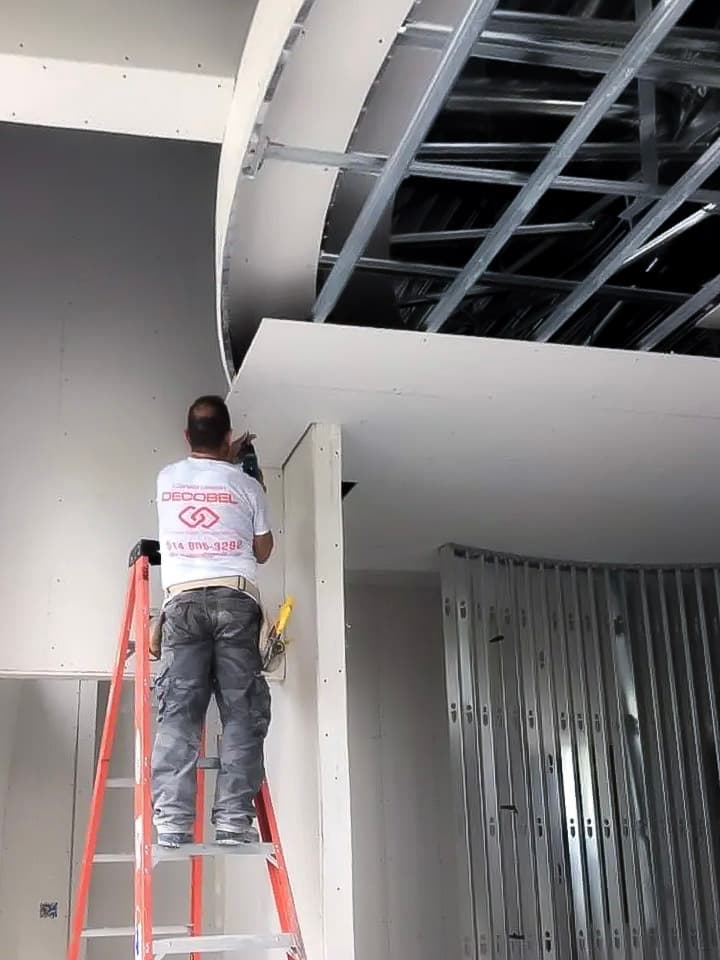 Worker installing drywall onto a metal framework in an interior finishing project.