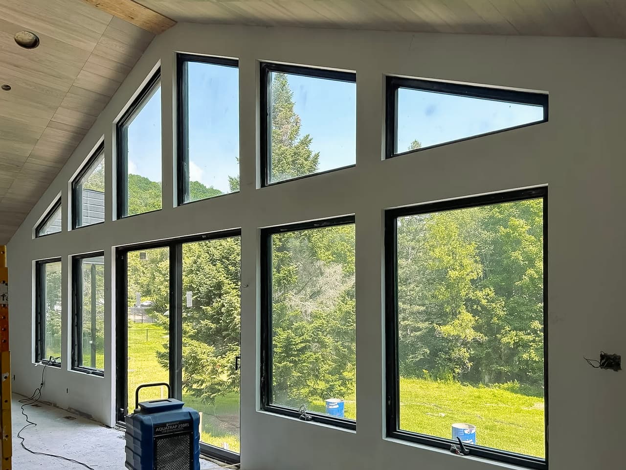 Interior of a house under construction with a large glass facade providing a panoramic view of nature.