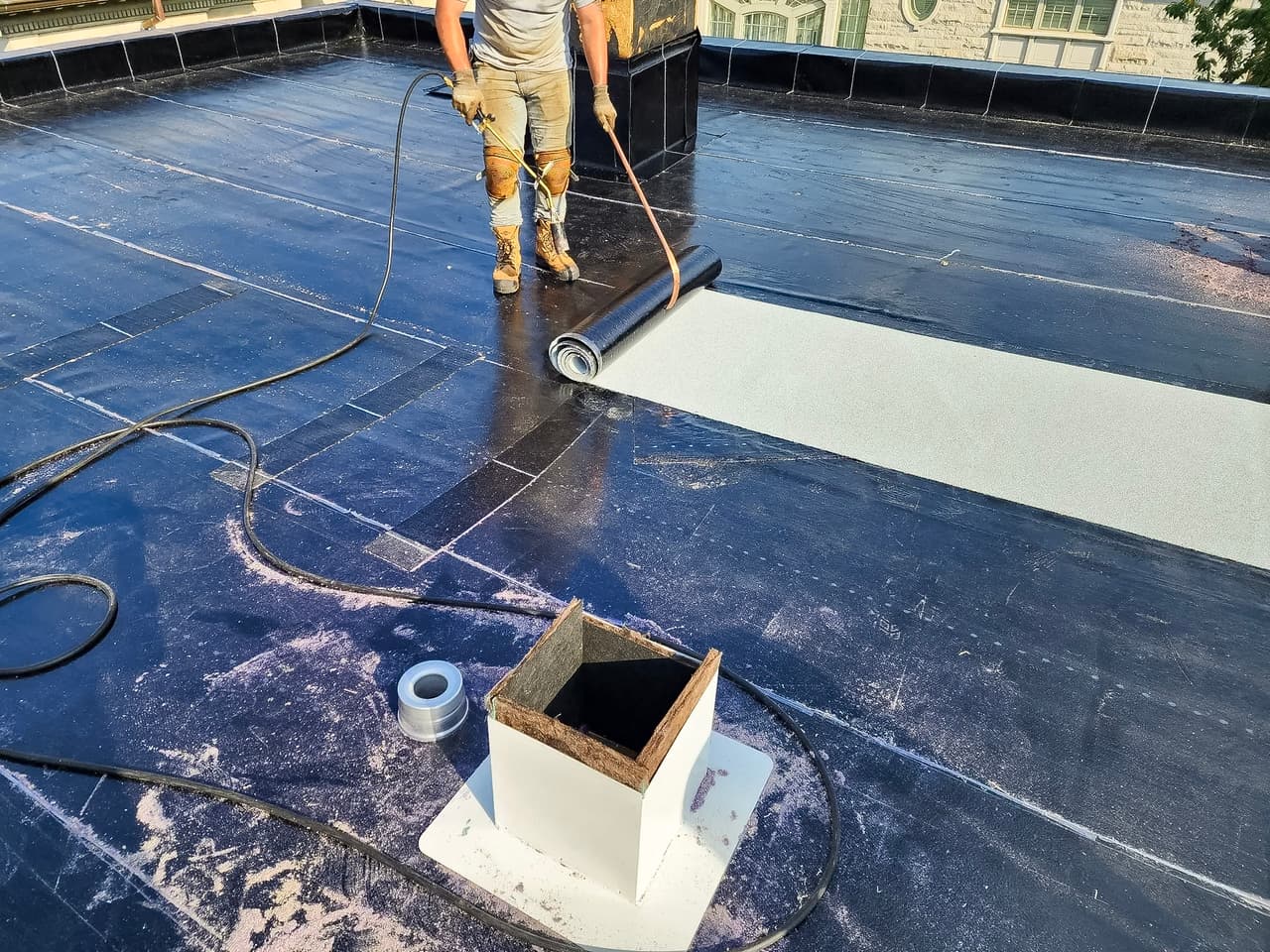 Installation work of an elastomeric membrane roof with a worker using a torch.