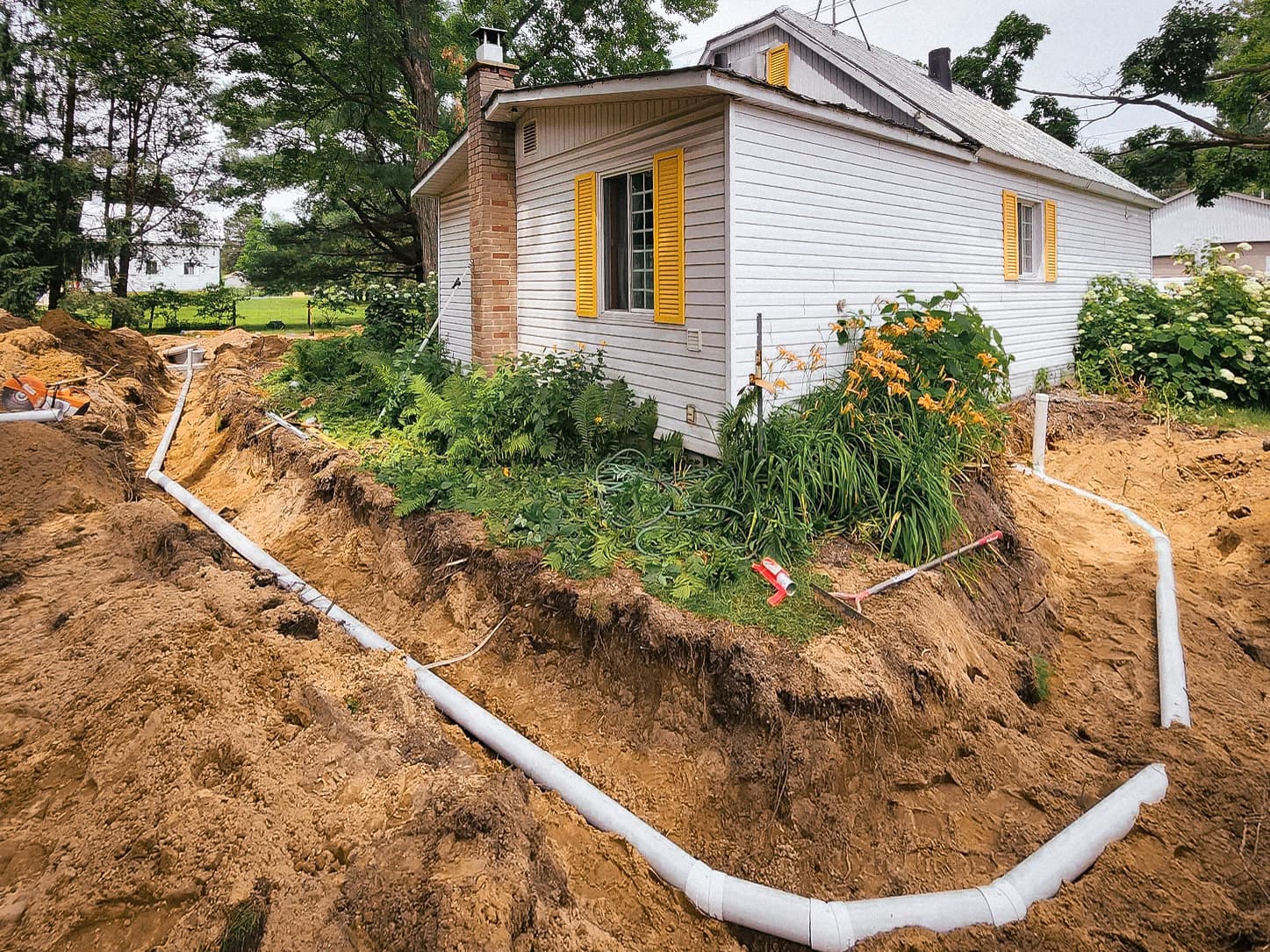 Drainage work around a single-family house with PVC pipe installation.