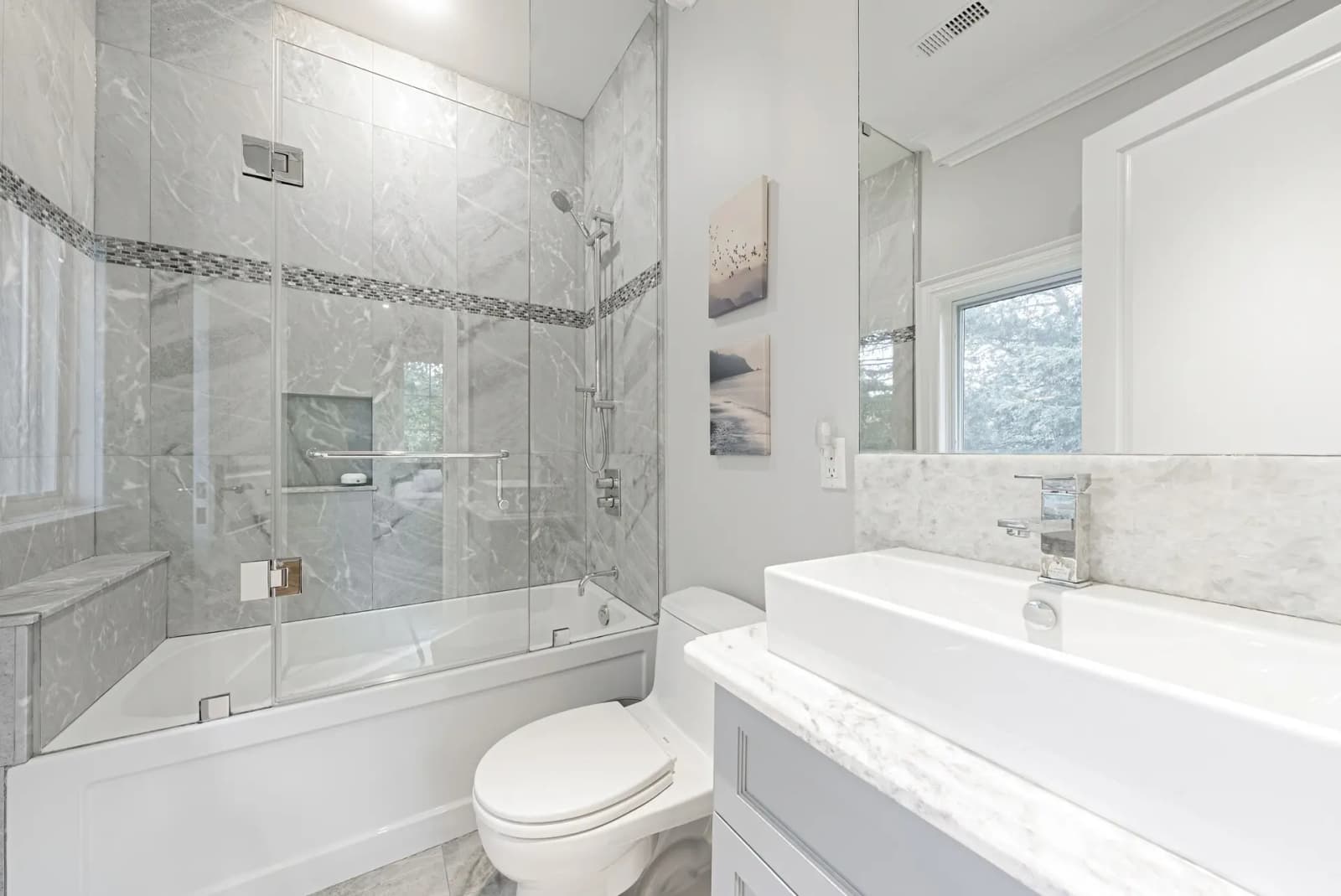 Elegant bathroom with a bathtub and shower separated by a glass partition, a floating vanity, and light gray marble tile.