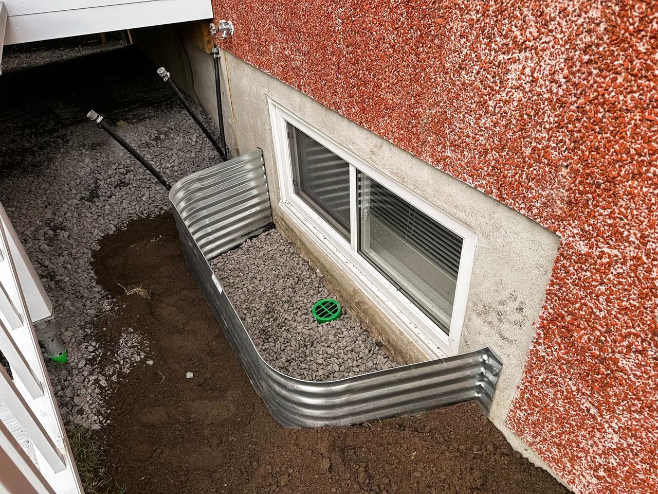 Metal window well installed in front of basement window with gravel drainage and protective grate