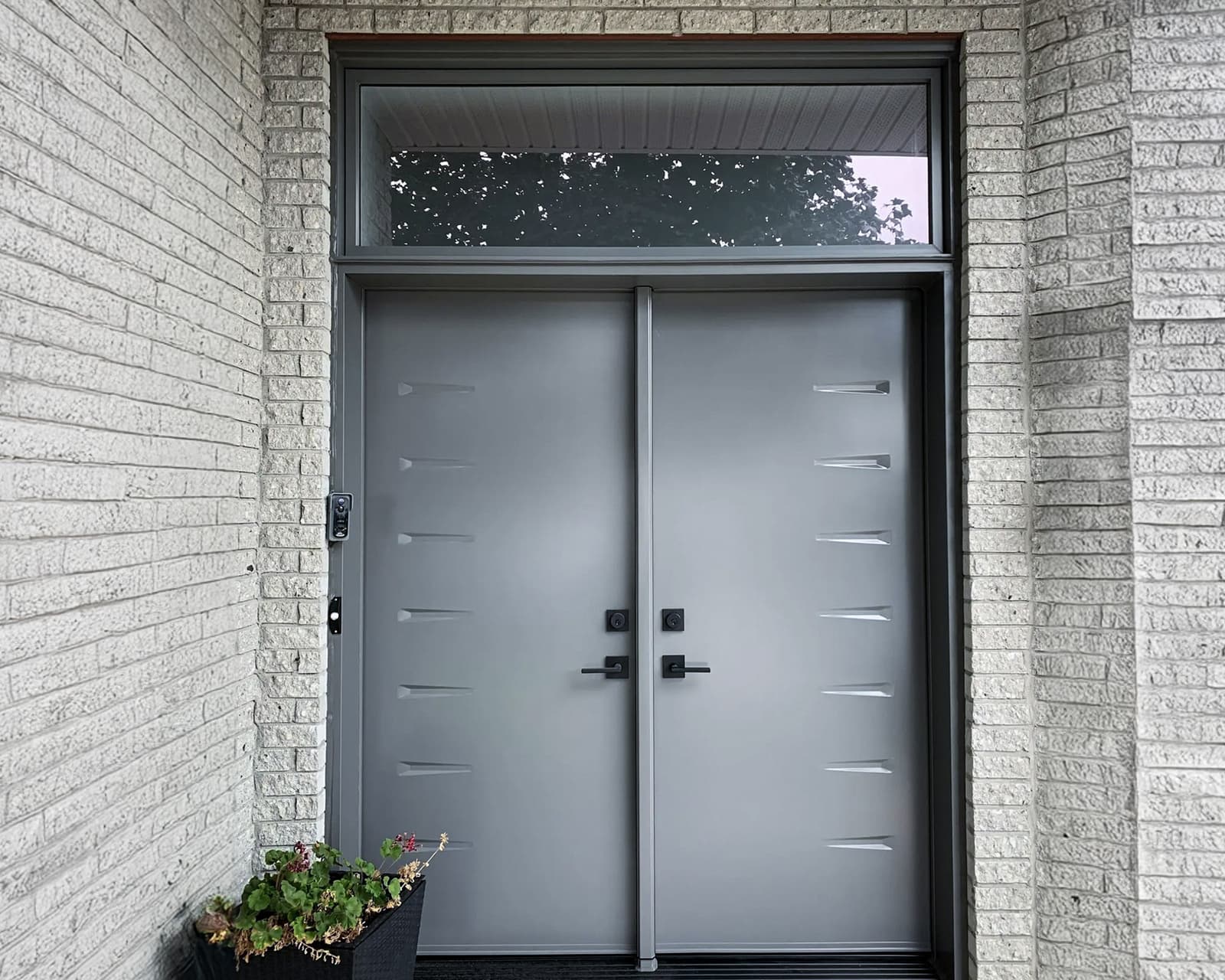 Modern double steel front door with black handles and upper glass panel in a contemporary home.