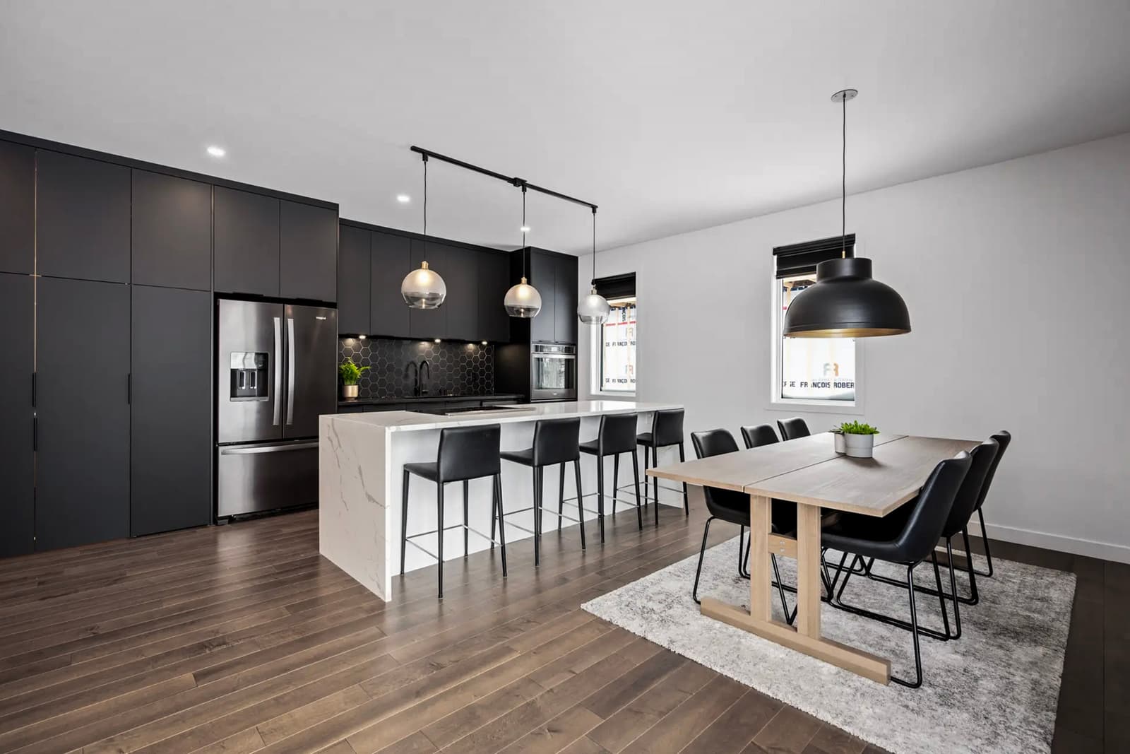 Modern kitchen with black cabinets, a marble island, and an elegant dining room with a wooden table.