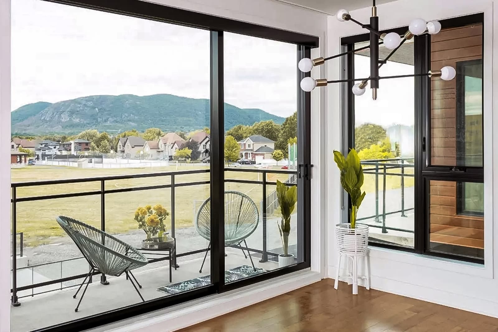 Modern sliding patio doors with a panoramic view of a balcony featuring furniture and mountains in the background.