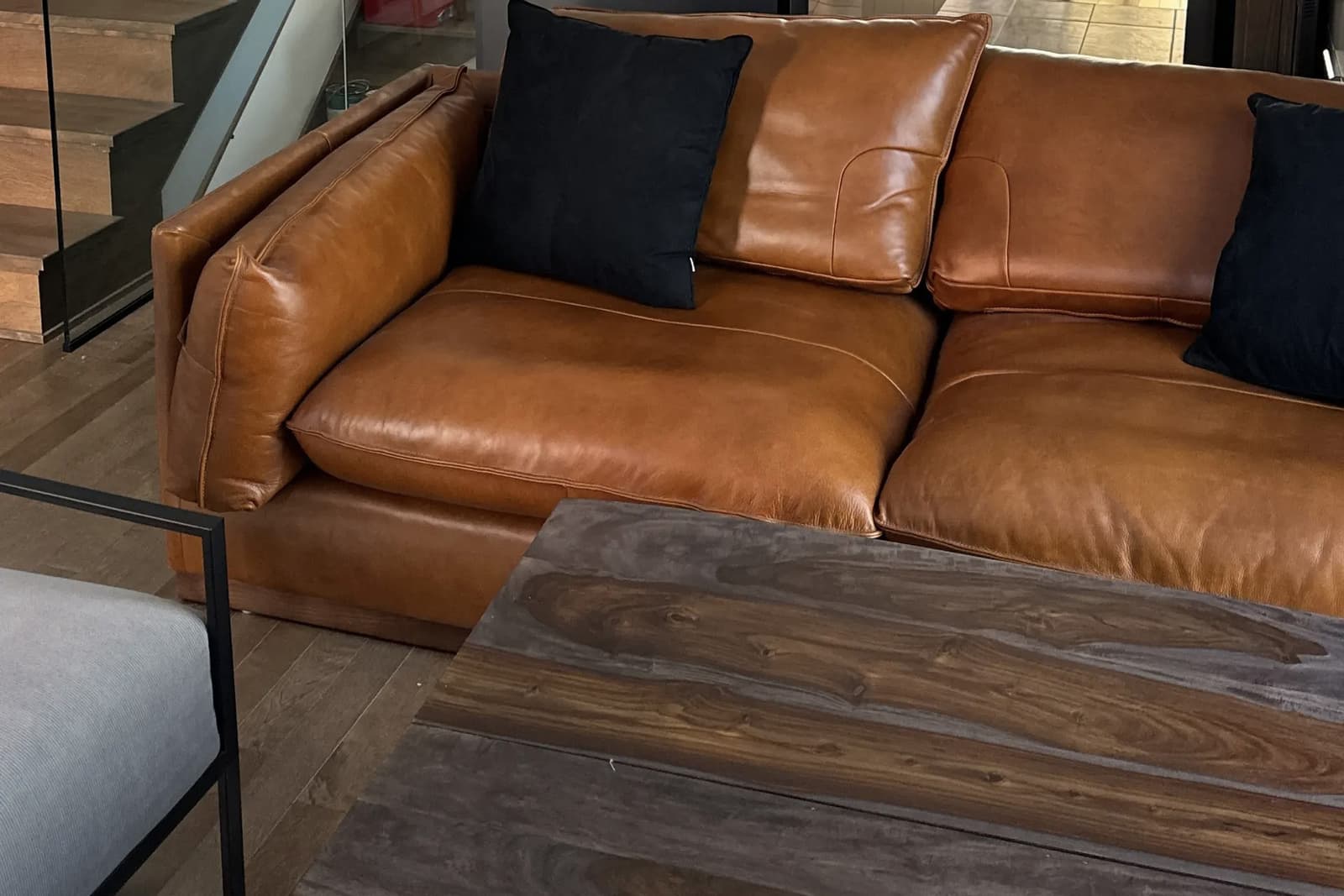 Close-up of a caramel leather sofa with black cushions, dark wooden coffee table, and natural wood flooring in a modern interior.