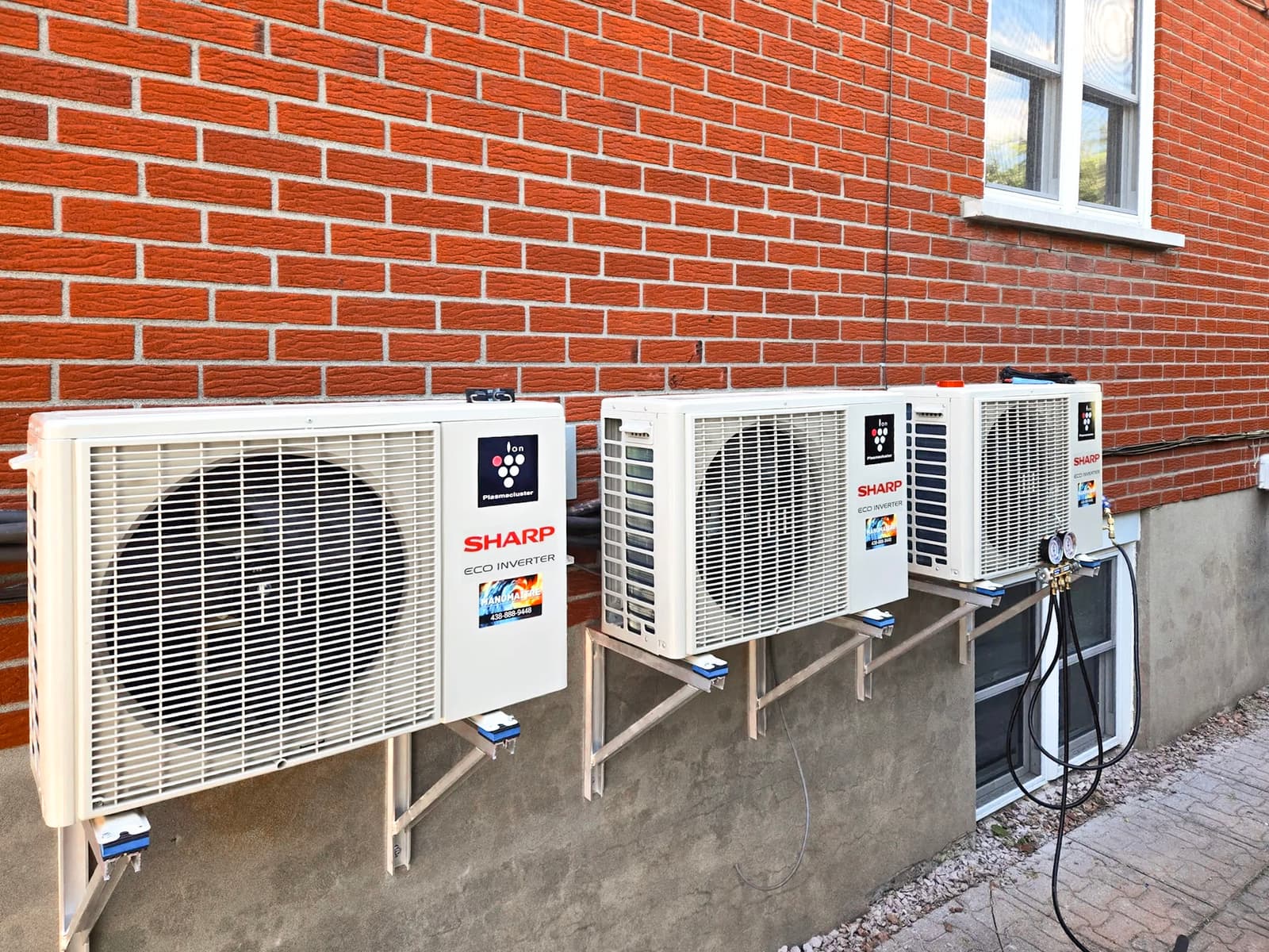 Installation of three Sharp wall-mounted outdoor air conditioning units on a red brick wall. A high-performance cooling solution for large homes.