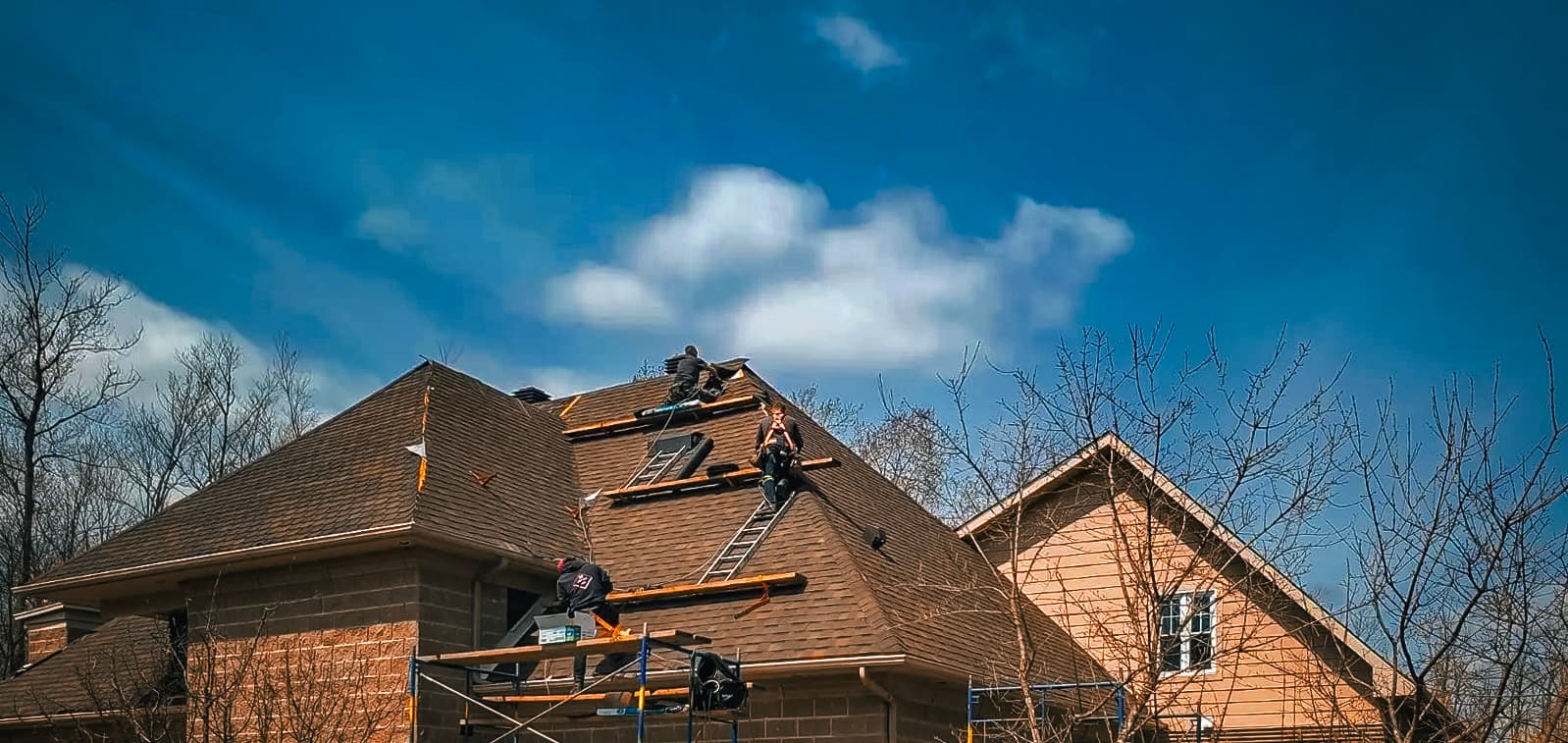Roofers working on a sloped roof under a blue sky, installing shingles and renovating a house.