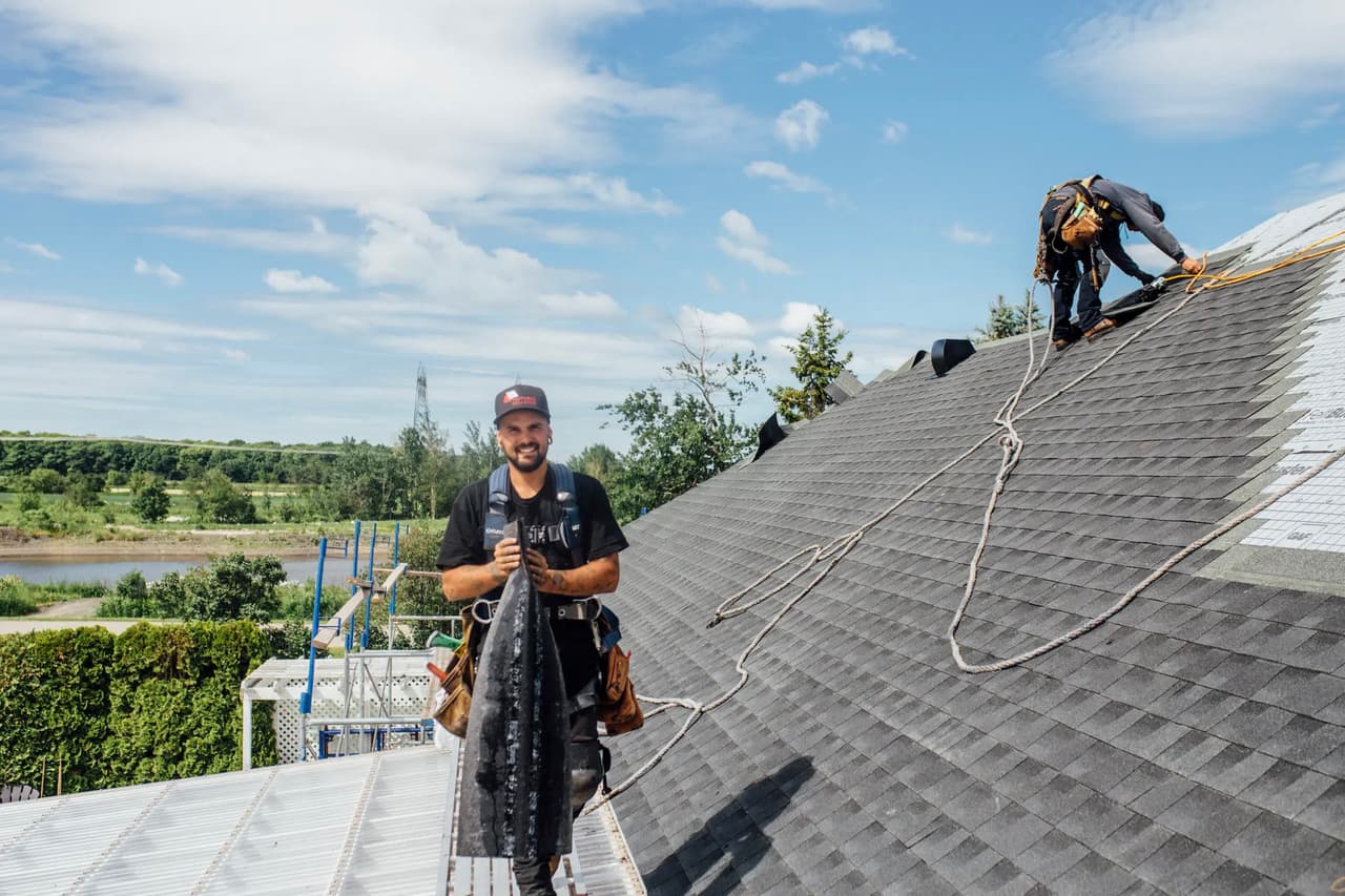 Workers installing a grey shingle roof on a house under a clear sky