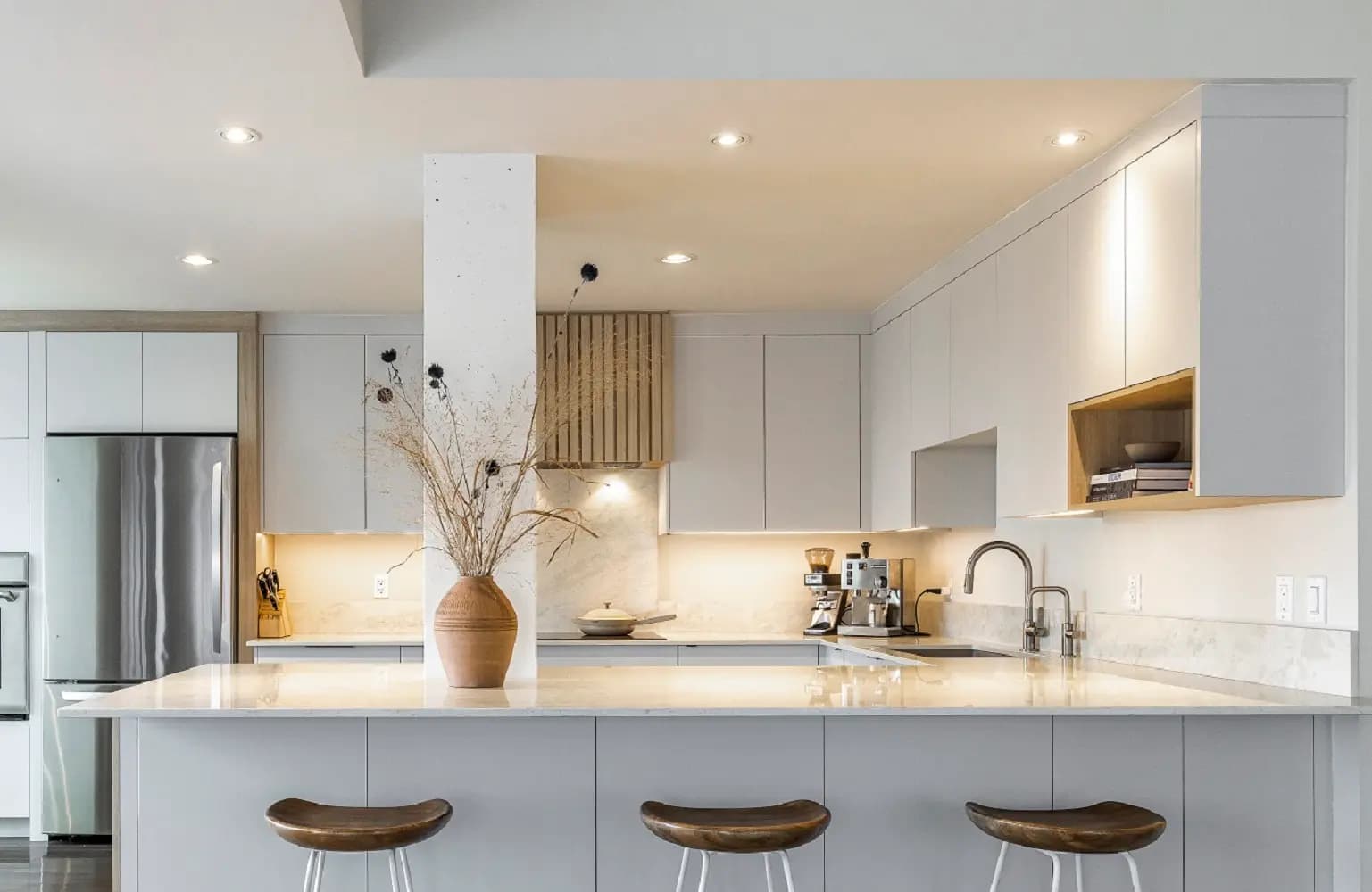 A minimalist, elegant kitchen combining white, natural wood and quartz. The contrast between materials creates a warm, modern ambience.