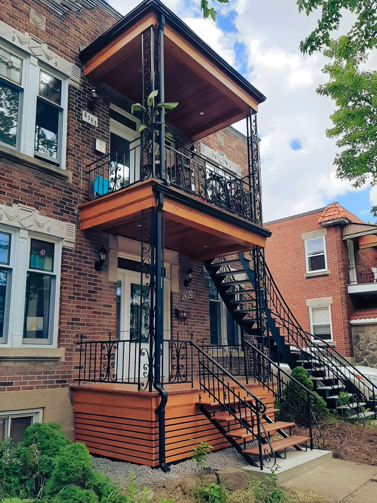 Montreal brick plex with renovated wooden balconies, black metal exterior stairs, and decorative railings.