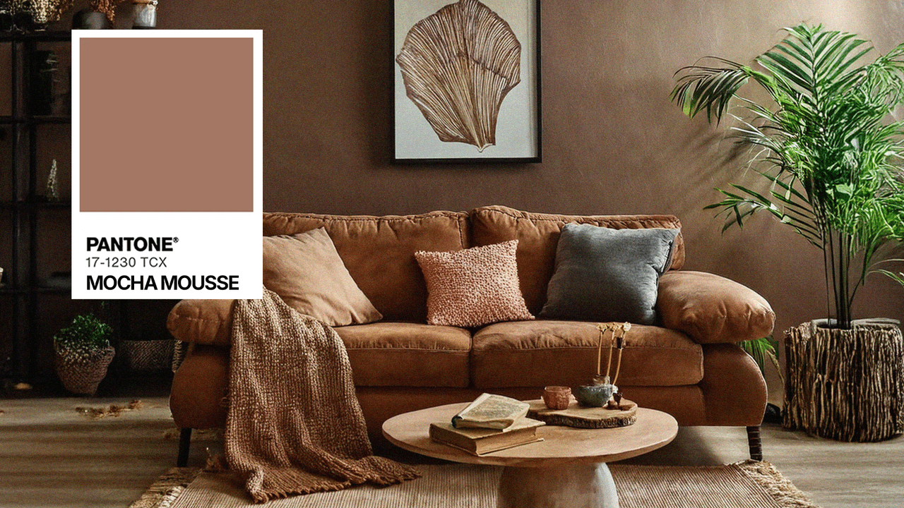 Cozy living room with brown velvet sofa, mocha mousse wall color, natural decor with green plant, textured pillows, and round wooden coffee table.