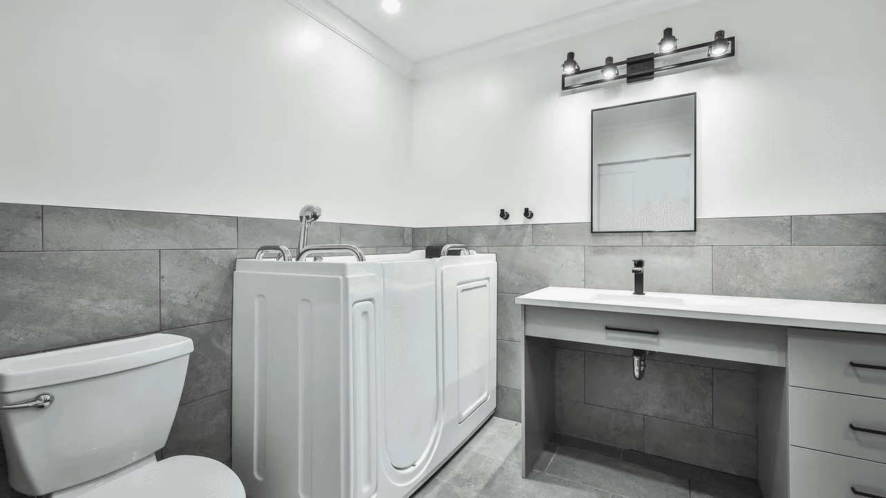 Kim Lacharité designer d'intérieur - Modern bathroom with walk-in therapeutic tub, wall-mounted sink and gray ceramic wall tiles