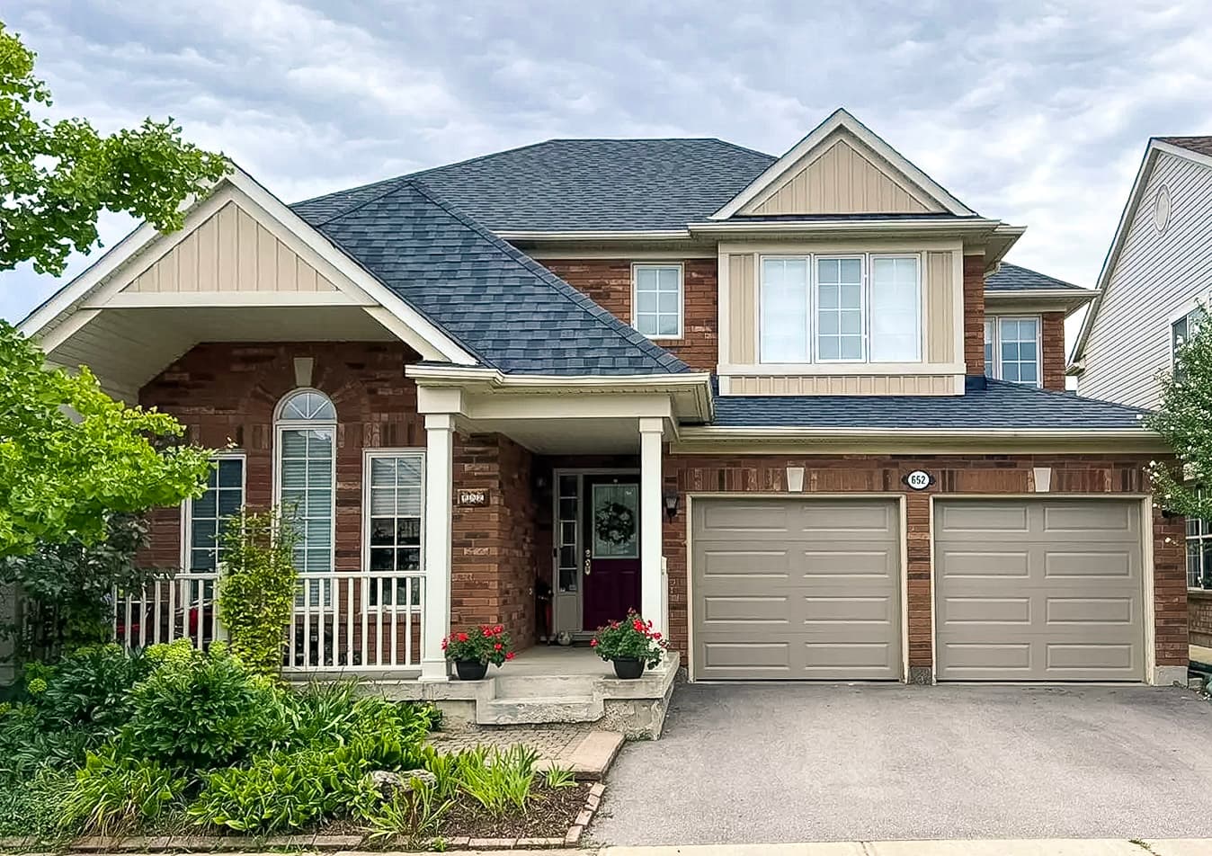 Brick family home with double garage, shingle roof, front porch, and well-maintained landscaping