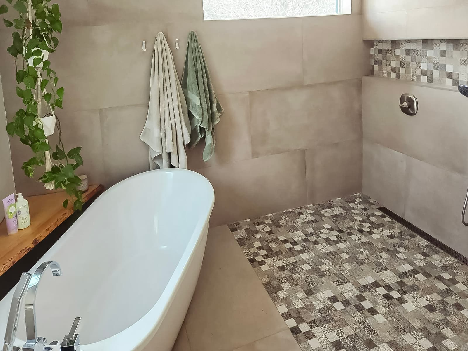 Modern bathroom with freestanding bathtub, walk-in shower, mosaic tile flooring, and natural plant decor.
