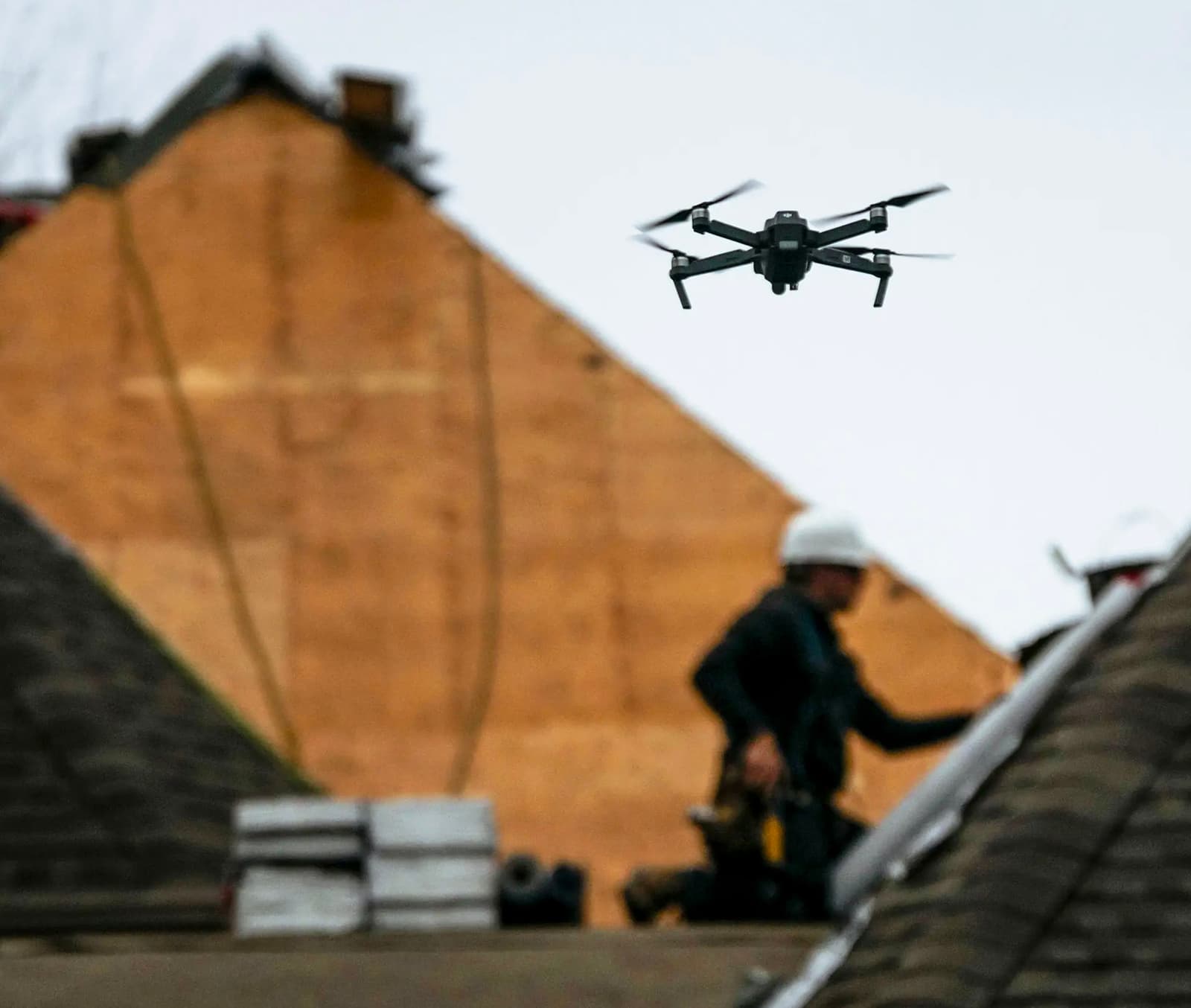 &nbsp;Drone flying above a roofing site where workers with helmets are performing renovations.