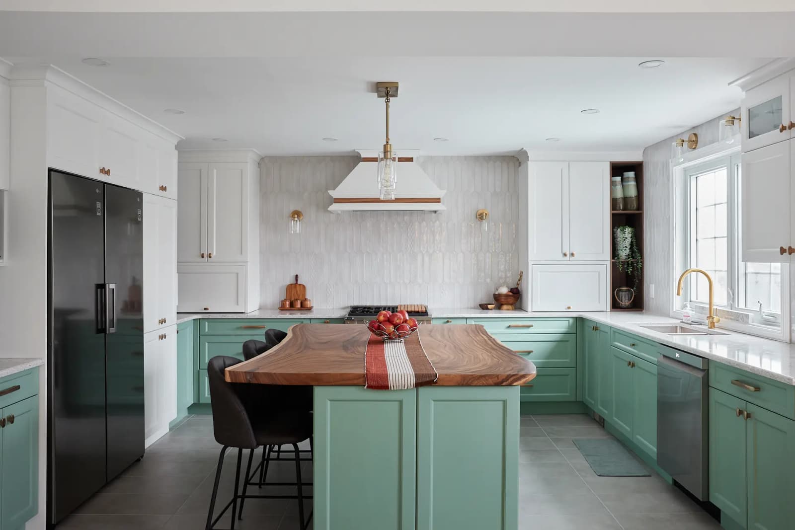 Transitional-style Montréal kitchen, featuring a natural veneer centre island with clean lines. Mint-green cabinetry and copper handles add a fresh, elegant touch to the space. The textured backsplash and neutral ceramic floor create an interesting contrast.