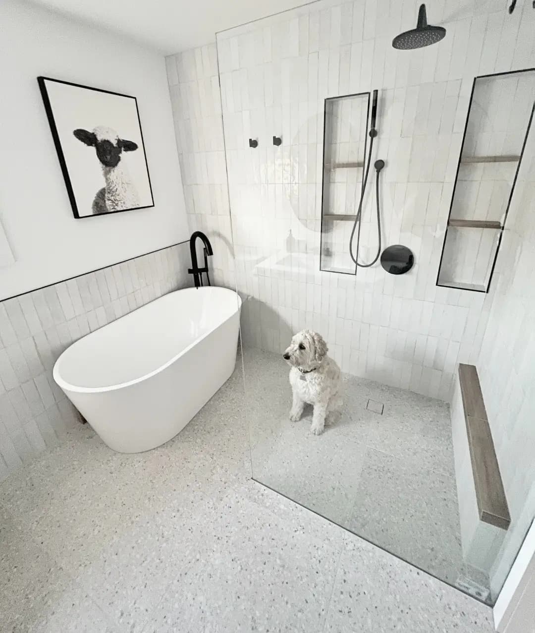 Modern bathroom with a freestanding bathtub, walk-in shower, and terrazzo tiles. Accompanied by a small dog.