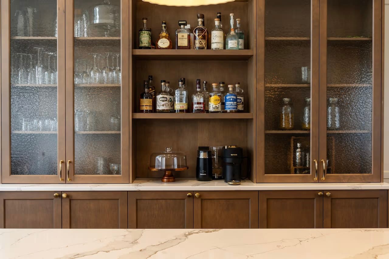 Dark wood bar cabinet with glass doors, liquor bottles, and small appliances.