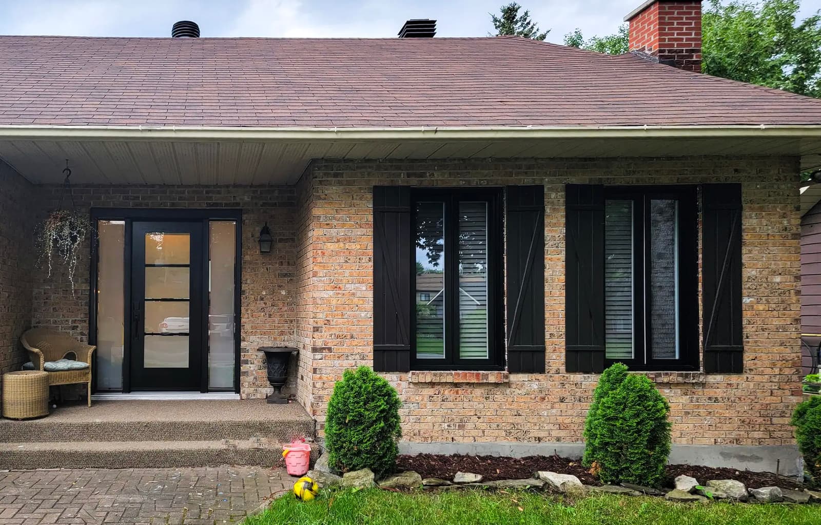 Brick house with a black glass door, matching shutters, and small front yard landscaping.<br>