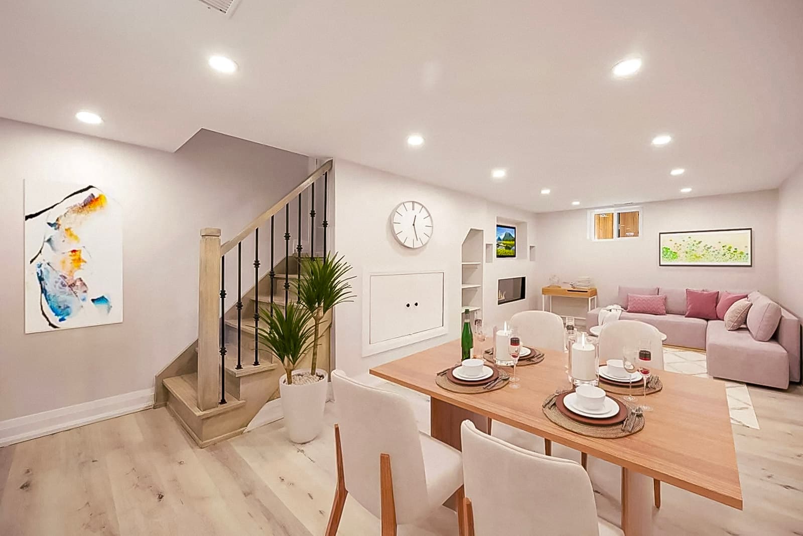 Finished basement with dining and living area, decorated in a modern style with a wooden staircase, white walls, and recessed lighting.