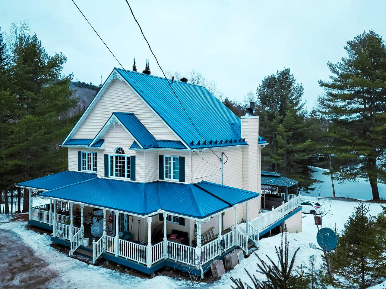 Renovated Victorian house with a blue metal roof and covered porch in winter.
